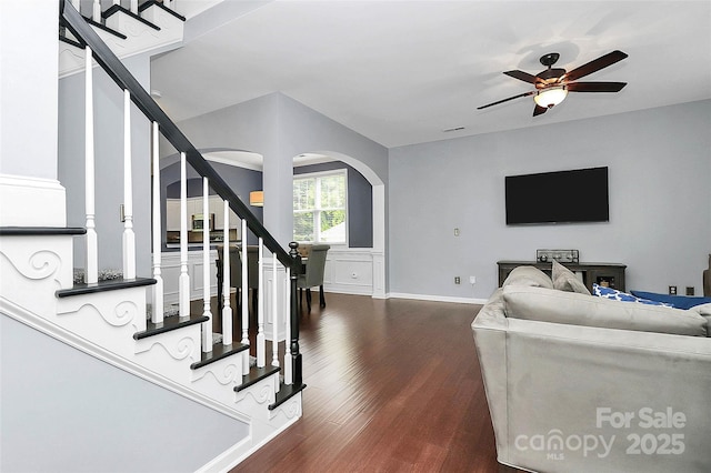 living room with dark wood-type flooring, stairway, ceiling fan, arched walkways, and baseboards