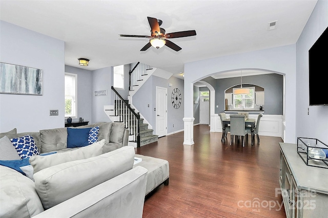 living room with arched walkways, dark wood-style flooring, ceiling fan, stairs, and healthy amount of natural light