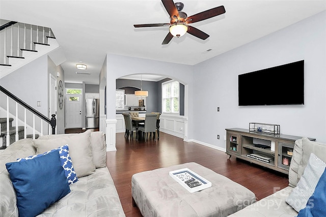 living area with arched walkways, dark wood-style floors, stairs, and a ceiling fan