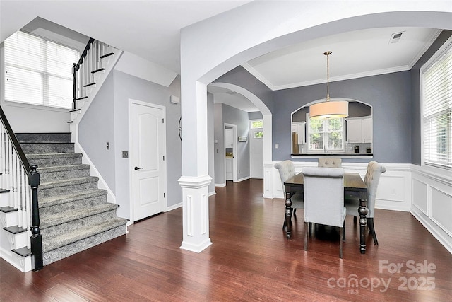 dining room featuring dark wood-type flooring, stairway, plenty of natural light, crown molding, and arched walkways