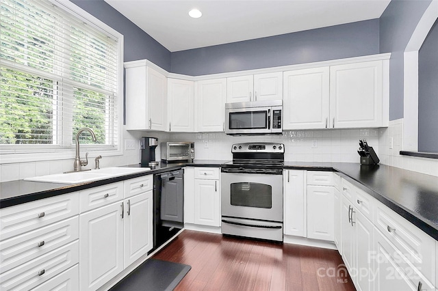 kitchen with appliances with stainless steel finishes, a sink, dark countertops, white cabinets, and recessed lighting