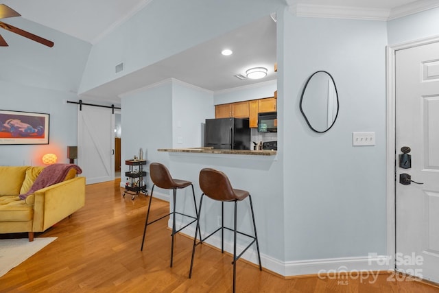 2502 Cranbrook Ln Unit 8, Charlotte, NC 28207 - kitchen featuring black appliances, a breakfast bar area, a barn door, light wood-style flooring, and crown molding