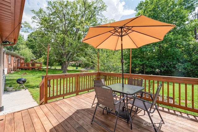 wooden terrace with outdoor dining area, a lawn, and view of wooded area