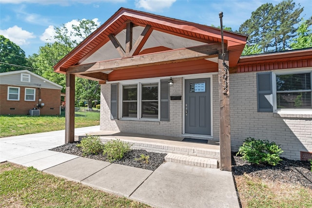 doorway to property featuring covered porch, brick siding, central AC unit, and a yard