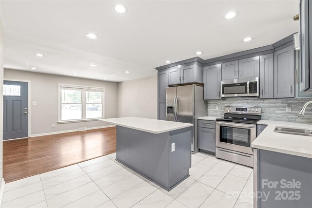 kitchen featuring stainless steel appliances, a sink, light countertops, gray cabinets, and recessed lighting