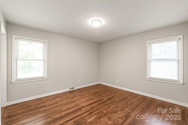 spare room with dark wood-style flooring, plenty of natural light, and baseboards