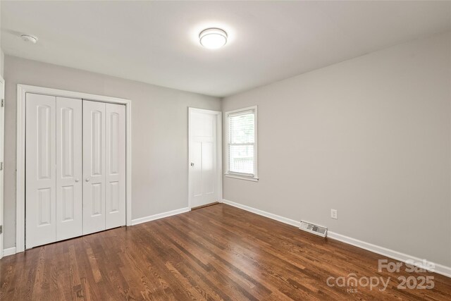 unfurnished bedroom featuring dark wood finished floors, baseboards, and a closet