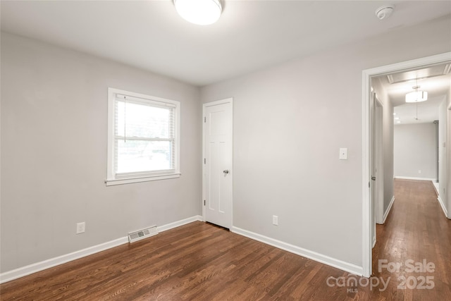 unfurnished bedroom featuring attic access, wood finished floors, and baseboards