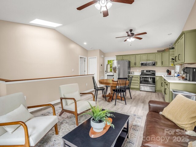 living area with ceiling fan, light wood-style flooring, lofted ceiling, a skylight, and baseboards