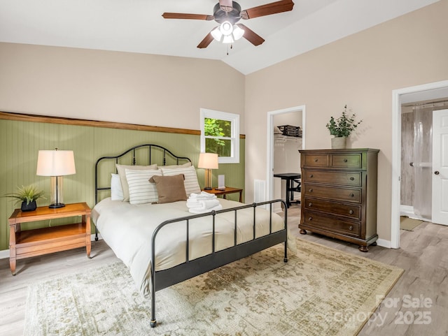 bedroom featuring wood finished floors, a walk in closet, baseboards, vaulted ceiling, and a closet