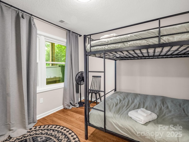 bedroom featuring wood finished floors, a textured ceiling, and baseboards