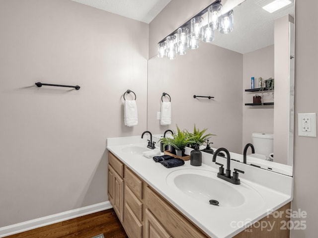 bathroom with wood finished floors, double vanity, toilet, and baseboards