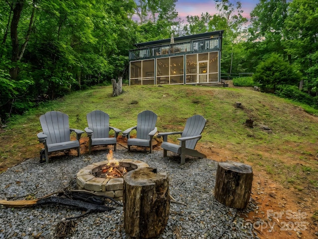 yard at dusk featuring a sunroom, an outdoor fire pit, and a lawn