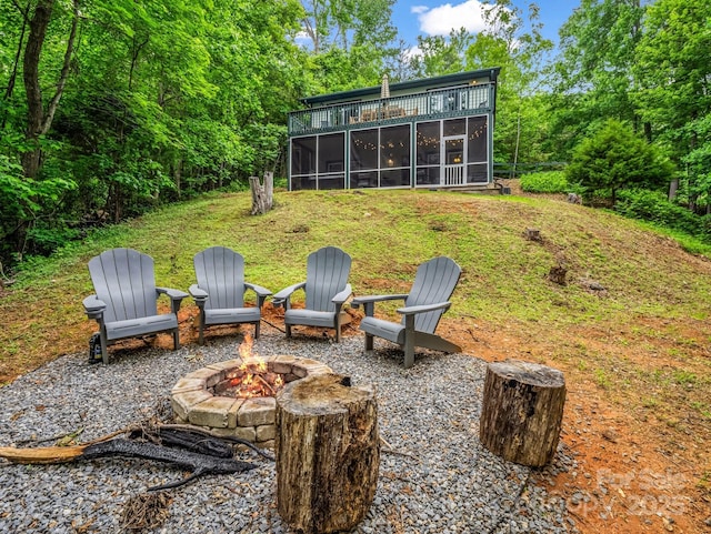 view of green lawn with a sunroom and an outdoor fire pit