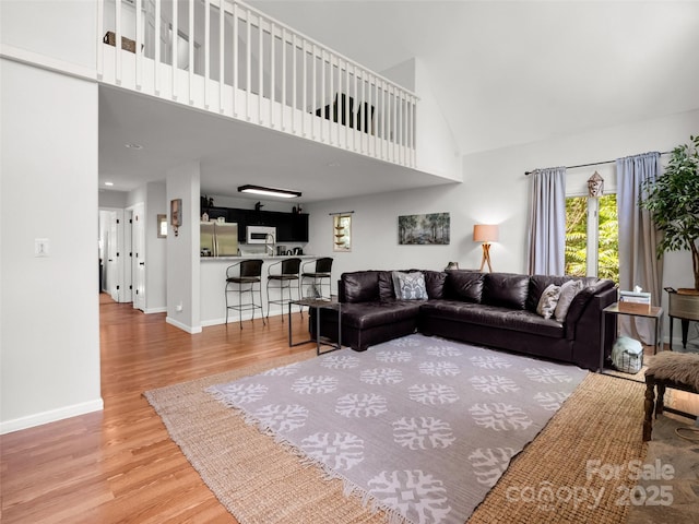 living area with high vaulted ceiling, wood finished floors, and baseboards