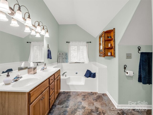 bathroom featuring a bath, vaulted ceiling, stone finish flooring, double vanity, and baseboards