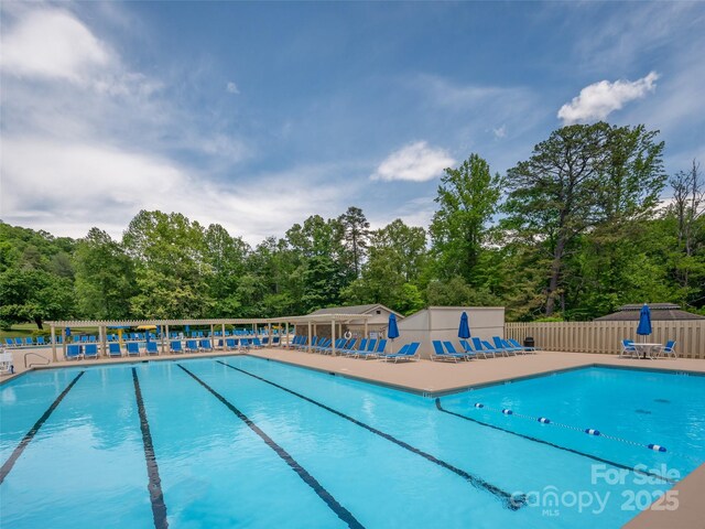 community pool featuring fence, a patio, and view of scattered trees