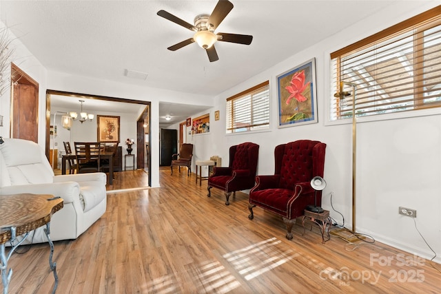 living room featuring light wood-style floors, a chandelier, ceiling fan, and baseboards