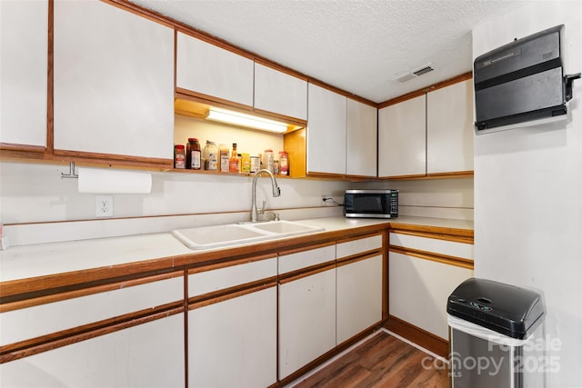 kitchen with stainless steel microwave, a sink, dark wood-type flooring, light countertops, and a textured ceiling
