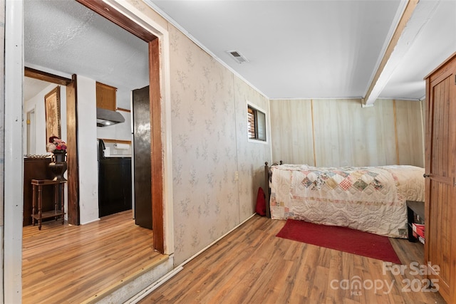 bedroom featuring wood finished floors, wallpapered walls, and freestanding refrigerator