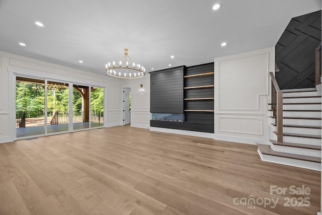 1408 Bloomsberry Ln, Waxhaw, NC 28173 - unfurnished living room with a decorative wall, light wood-style flooring, stairs, recessed lighting, and a chandelier