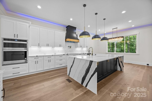 1408 Bloomsberry Ln, Waxhaw, NC 28173 - kitchen with custom exhaust hood, white cabinets, double oven, a large island, and light wood-style floors