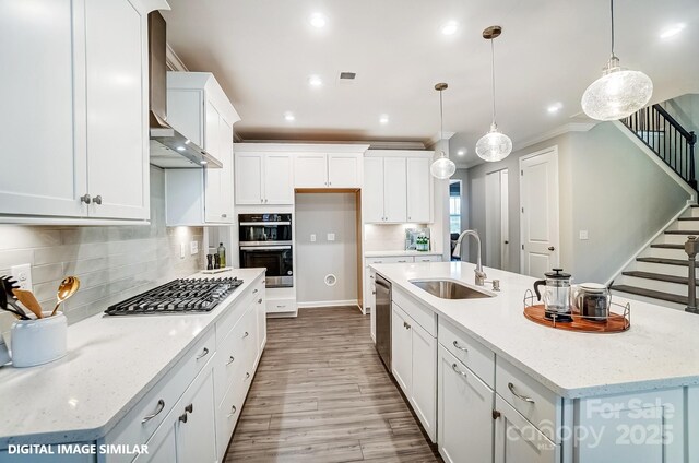 kitchen featuring a sink, stainless steel appliances, an island with sink, wood finished floors, and white cabinets
