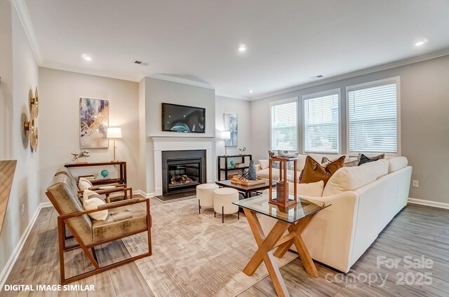 living area with ornamental molding, a glass covered fireplace, light wood-type flooring, baseboards, and recessed lighting