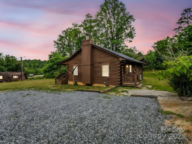 property exterior at dusk with log exterior, a chimney, a deck, and crawl space