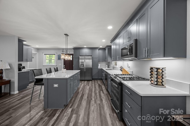 kitchen with appliances with stainless steel finishes, gray cabinets, a breakfast bar, a center island, and dark wood finished floors