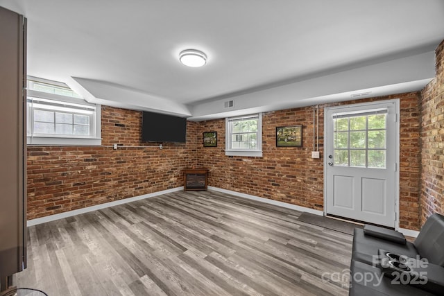 unfurnished living room with brick wall, baseboards, and wood finished floors