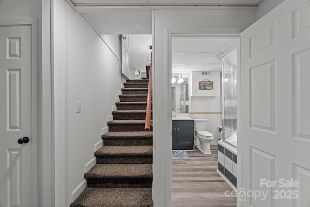 stairway with a paneled ceiling, wood finished floors, and baseboards