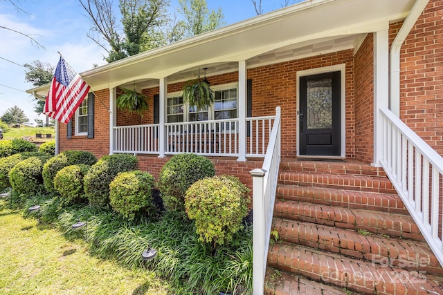 view of exterior entry featuring brick siding and covered porch