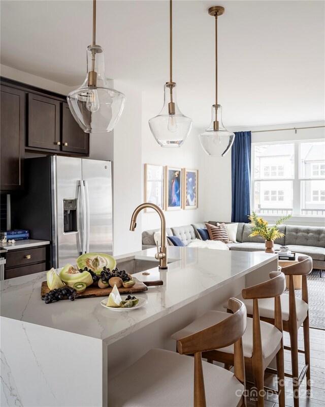 kitchen with stainless steel fridge, open floor plan, a kitchen breakfast bar, dark brown cabinetry, and light stone counters