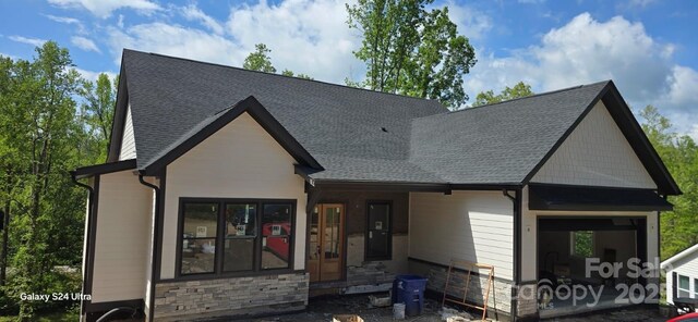 view of front facade featuring stone siding and a shingled roof