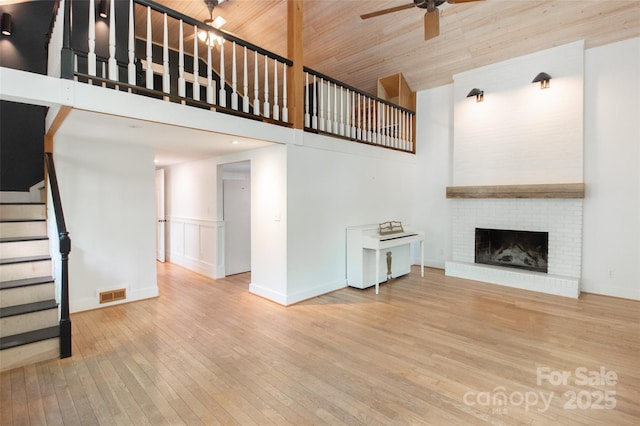 37 Geneva Cir Unit 1/2, Franklin, NC 28734 - unfurnished living room featuring a towering ceiling, a ceiling fan, stairway, wood-type flooring, and a brick fireplace