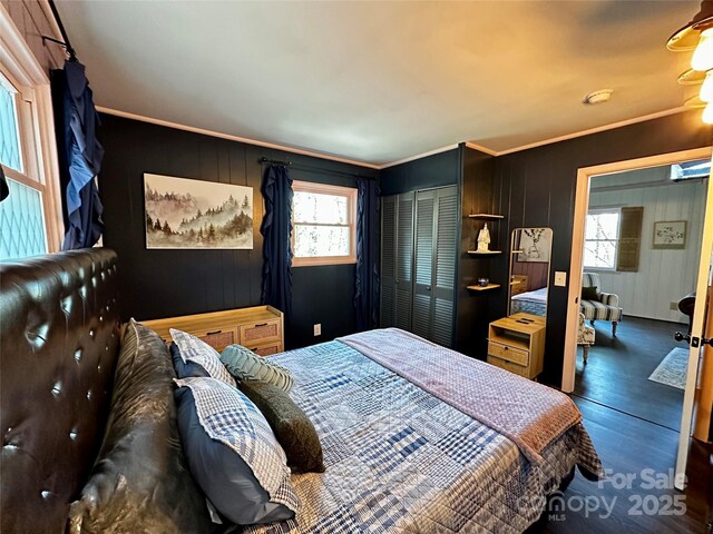 bedroom with a closet, wood finished floors, ornamental molding, and wooden walls