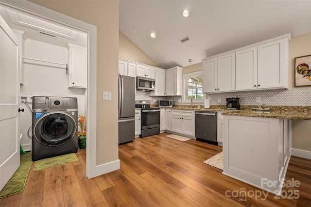 105 Kingston Pl, Spindale, NC 28160 - kitchen featuring washer / clothes dryer, appliances with stainless steel finishes, white cabinets, wood finished floors, and vaulted ceiling