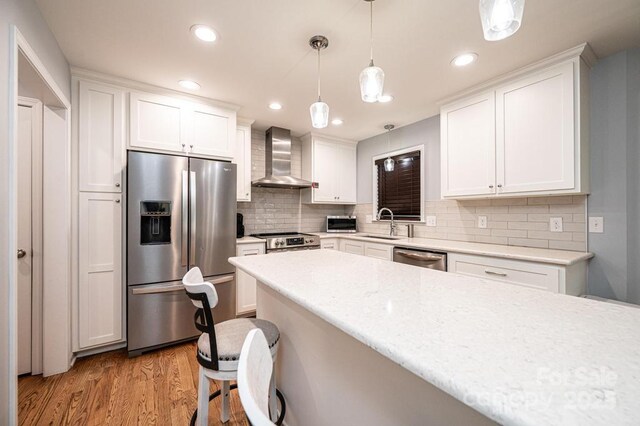kitchen with stainless steel appliances, wall chimney exhaust hood, a sink, light wood-style flooring, and white cabinets