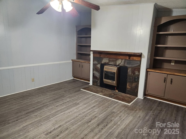 unfurnished living room featuring heating unit, wood finished floors, ceiling fan, a wainscoted wall, and wood walls