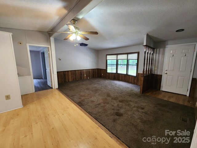 empty room featuring ceiling fan, wooden walls, wainscoting, wood finished floors, and a textured ceiling