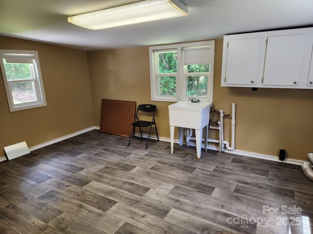 clothes washing area featuring dark wood finished floors, plenty of natural light, baseboards, and cabinet space