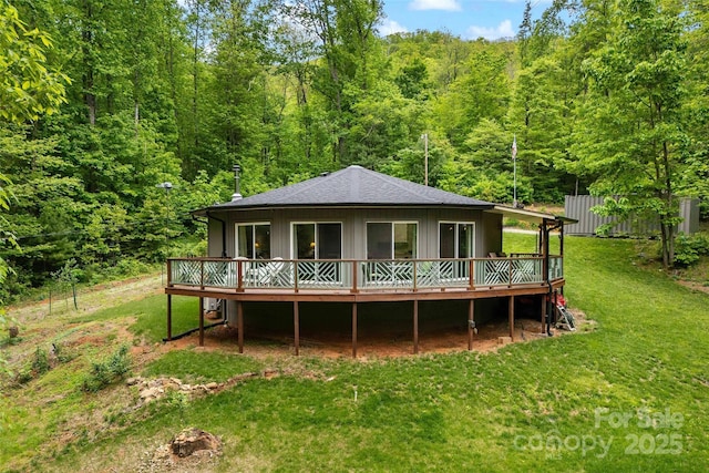 back of house featuring a deck, a view of trees, and roof with shingles