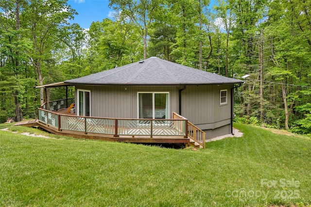 rear view of property featuring a shingled roof, a lawn, and a deck