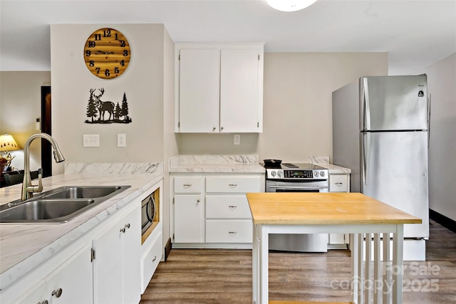 kitchen with a sink, stainless steel appliances, wood finished floors, and white cabinets
