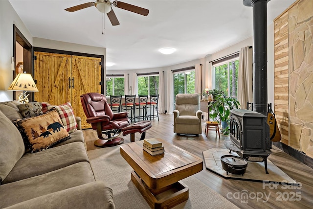 living area featuring a wood stove, healthy amount of natural light, a ceiling fan, and wood finished floors