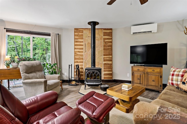 living room with a wall mounted AC, a wood stove, wood finished floors, and a ceiling fan