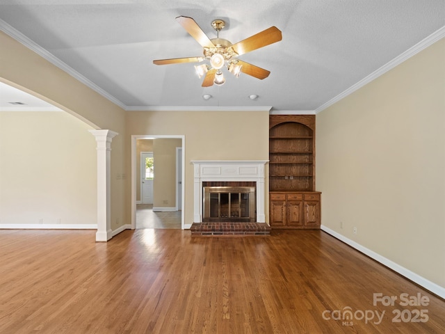 unfurnished living room with wood finished floors, ornate columns, a ceiling fan, baseboards, and ornamental molding