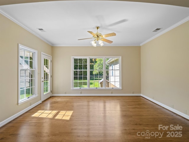 spare room with ornamental molding, plenty of natural light, wood finished floors, and baseboards