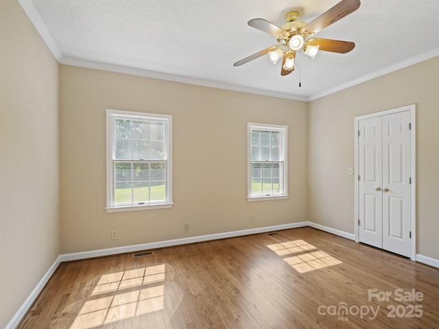spare room with healthy amount of natural light, ornamental molding, wood finished floors, ceiling fan, and baseboards